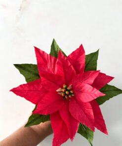 Flor de Pascua roja de papel crepé sostenida con una mano, con hojas verdes y detalles del centro floral.