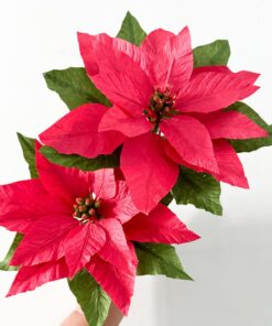 Dos Flores de Pascua rojas hechas a mano con papel crepé y hojas verdes sobre fondo blanco.