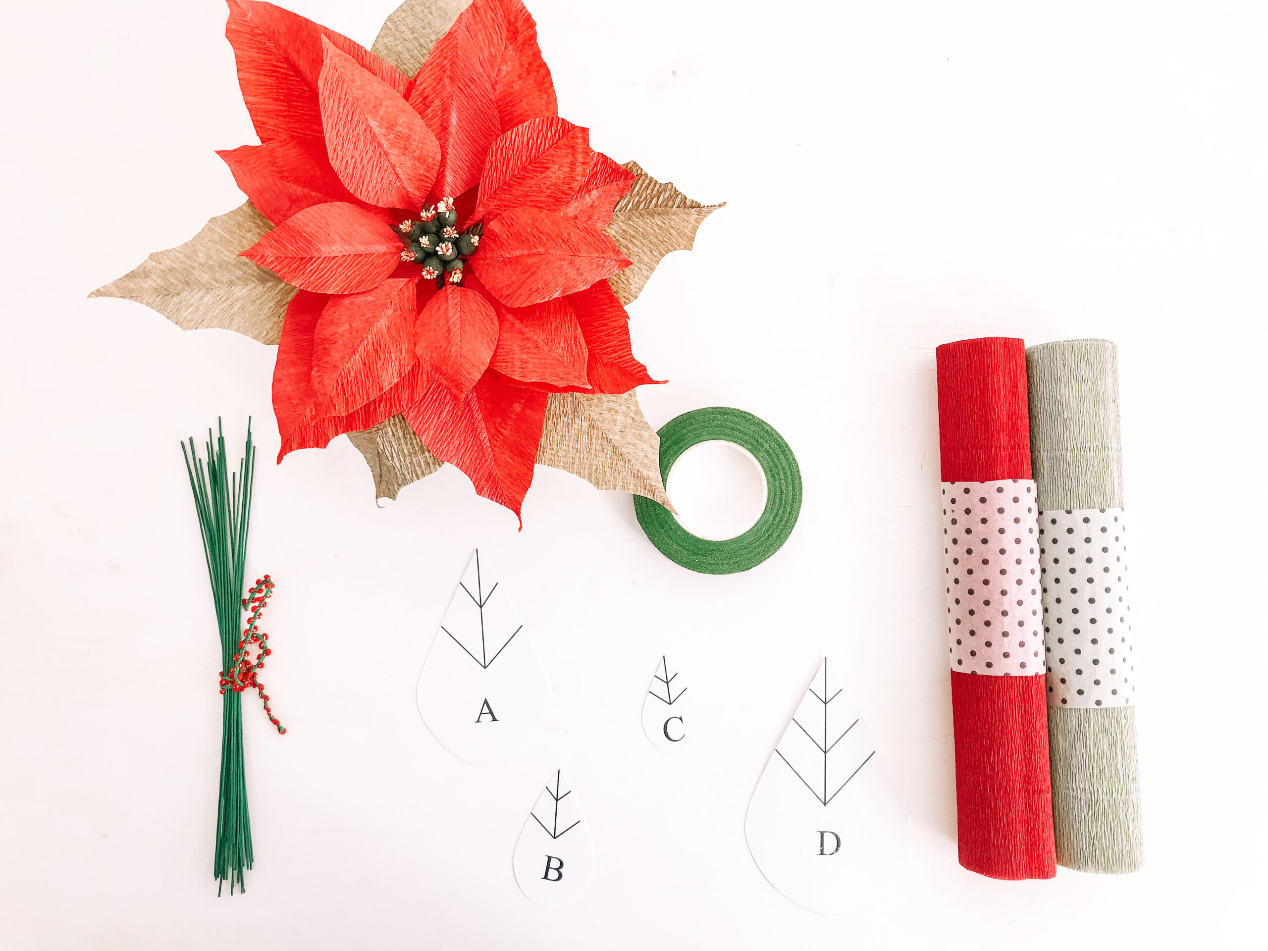 Flor de Pascua roja de papel junto a rollos de papel crepé, alambres, cinta floral y plantillas.